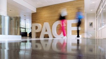 Two people walk past large white letters spelling the word 'PACE' in a modern lobby.