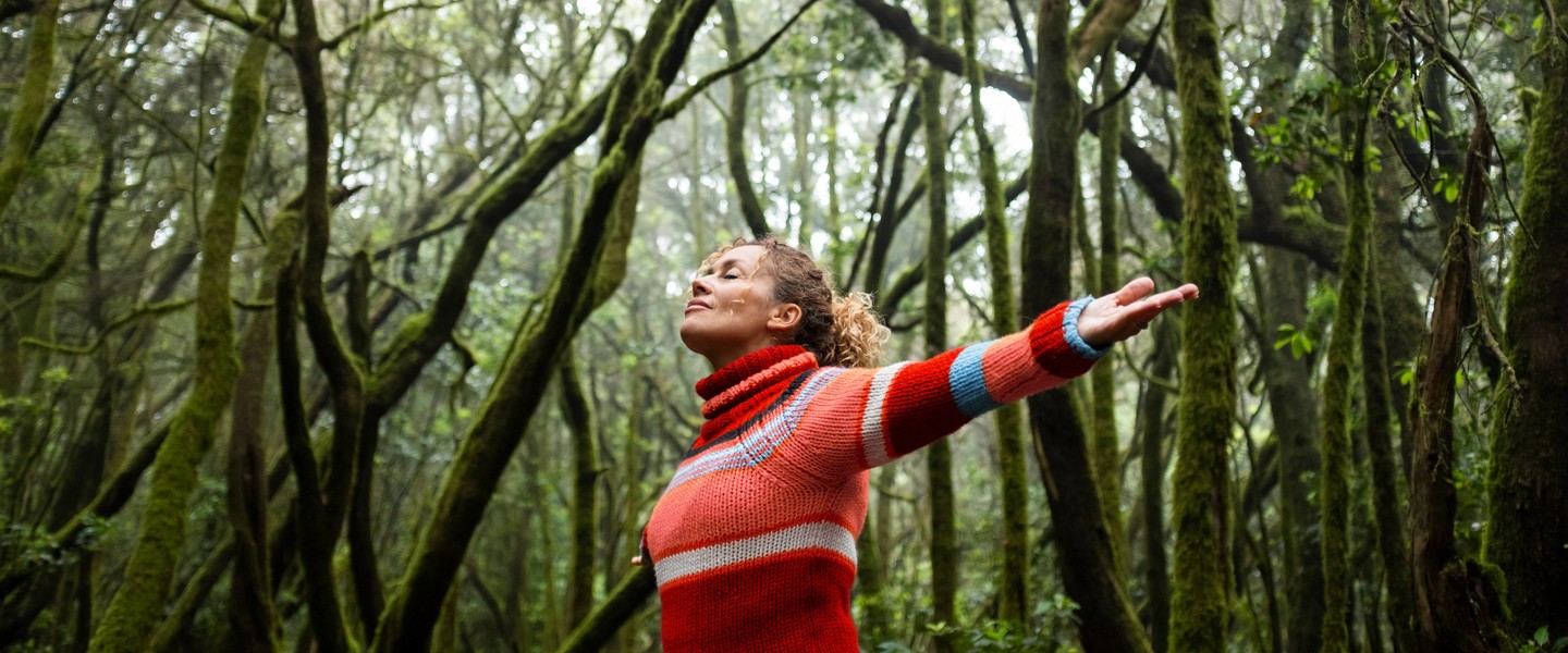 A woman with outstretched arms in a dense, misty forest, wearing a red and white sweater.