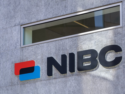 NIBC logo displayed on a gray wall, featuring blue and red elements next to the name in black letters.