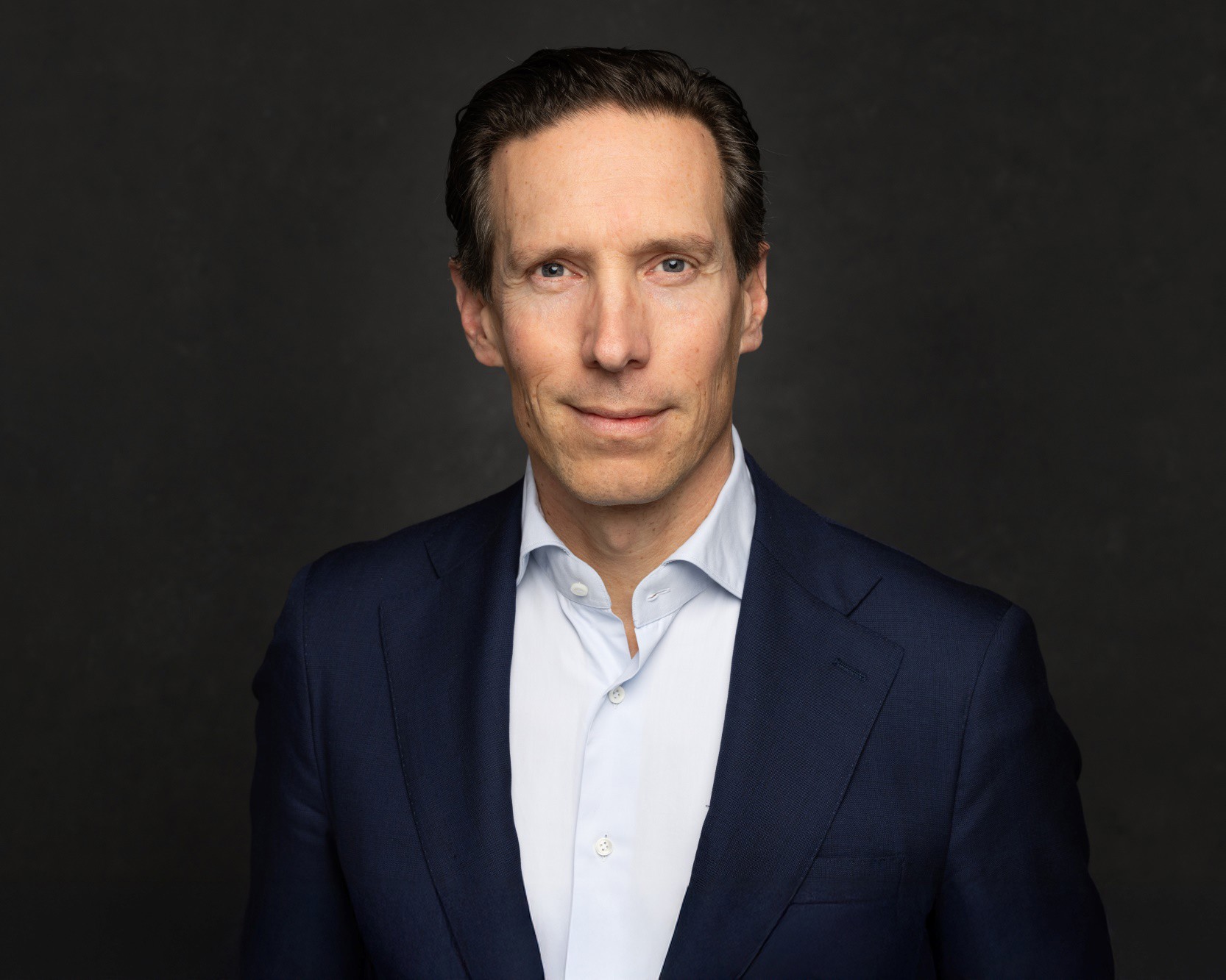 Sven in a dark blue blazer against a black-gray background, with a neutral expression.