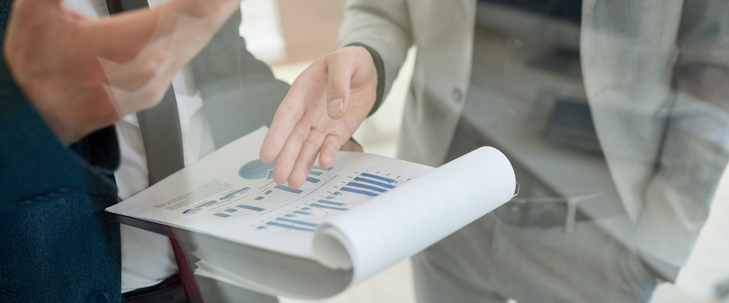 Two people are discussing graphs and figures on a document during a meeting.