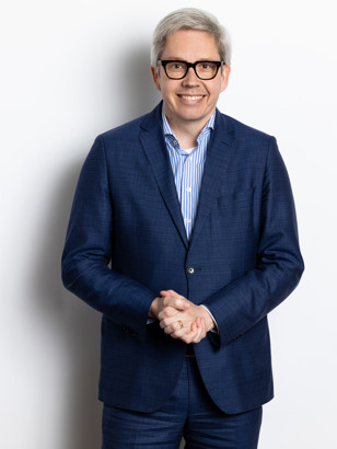 Toine in a blue suit with crossed arms, standing against a neutral white background.